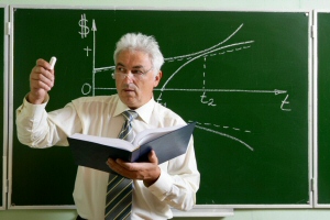 Older teacher demonstrating a point in front of a chalkboard.